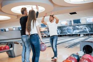 Gib mir High Five. Junge, fröhliche Freunde haben an ihren Wochenenden Spaß im Bowlingclub foto