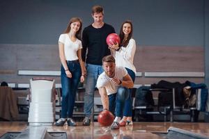 bereit zu werfen. Junge, fröhliche Freunde haben an ihren Wochenenden Spaß im Bowlingclub foto