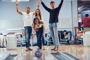 schöner Wurf. Junge, fröhliche Freunde haben an ihren Wochenenden Spaß im Bowlingclub foto