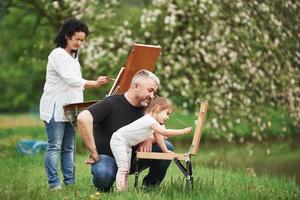 Erlernen dieser Kunst. großmutter und großvater haben spaß im freien mit enkelin. Malerei Konzeption foto