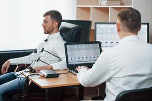 Wenn Sie verstanden haben, dass der Mann Probleme in Ihrem Geschäft macht. Verdächtiger Mann passiert Lügendetektor im Büro. Fragen stellen. Polygraph-Test foto