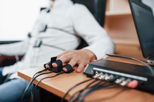 fokussiertes Foto. Verdächtiger Mann passiert Lügendetektor im Büro. Fragen stellen. Polygraph-Test foto