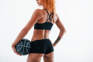 posieren für eine Kamera mit Fußball. Partikelansicht. Rothaarige Bodybuilderin ist im Studio auf weißem Hintergrund foto