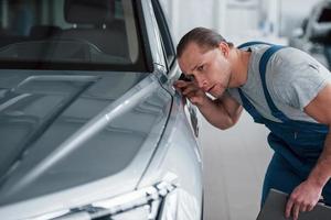 alles muss perfekt sein. nach fachmännischer Reparatur. Mann, der ein perfekt poliertes, silberfarbenes Auto betrachtet foto