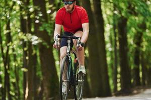 schöner Hintergrund. Radfahrer auf dem Fahrrad ist an sonnigen Tagen auf der Asphaltstraße im Wald foto