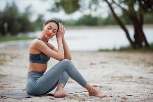 sich auf Übungen vorbereiten. brünette mit schöner körperform in sportlicher kleidung haben einen fitnesstag am strand foto