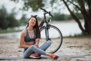 müssen sich erholen. Radfahrerin mit guter Körperform, die tagsüber neben ihrem Fahrrad am Strand sitzt foto