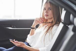 natürliche Beleuchtung. schönes blondes mädchen, das im neuen auto mit modernem schwarzem interieur sitzt foto