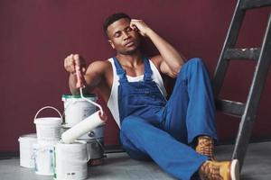 müde und schläfrig. junger afroamerikanischer arbeiter in blauer uniform macht eine pause bei seiner arbeit foto
