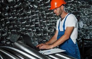 mit Laptop. Mann in Uniform arbeitet an der Produktion. Industrielle moderne Technologie foto