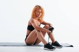 ruht auf der Rollmatte. Rothaarige Bodybuilderin ist im Studio auf weißem Hintergrund foto