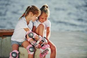 Zwei kleine Mädchen mit Rollschuhen im Freien in der Nähe des Sees im Hintergrund foto