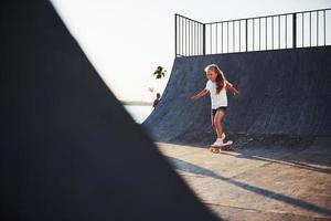 sonniger Tag. kind viel spaß mit skate an der rampe. fröhliches kleines Mädchen foto