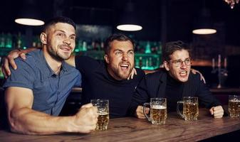 drei Sportfans in einer Bar beim Fußball schauen. mit Bier in der Hand foto