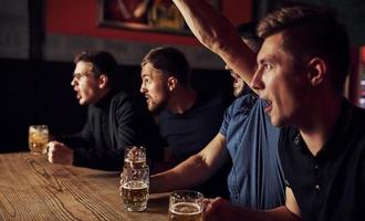 drei Sportfans in einer Bar beim Fußball schauen. mit Bier in der Hand foto