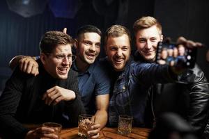 modernes Smartphone. Foto machen. freunde ruhen sich mit alkohol in den händen in der kneipe aus. Gespräch haben