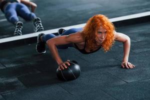 Liegestütze mit Ball machen. Sportliches rothaariges Mädchen hat tagsüber einen Fitnesstag im Fitnessstudio. muskulöser Körpertyp foto