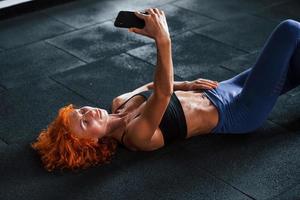 ein selfie mit dem telefon machen. Sportliches rothaariges Mädchen hat tagsüber einen Fitnesstag im Fitnessstudio. muskulöser Körpertyp foto