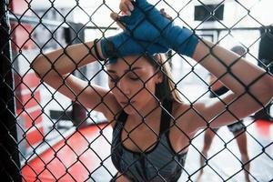 eine Pause machen. Sportlerin im Boxring hat Bewegung. an den Zaun gelehnt foto