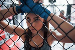 eine Pause machen. Sportlerin im Boxring hat Bewegung. an den Zaun gelehnt foto