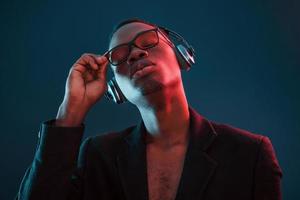 Genießen Sie das Hören von Musik in Kopfhörern. in Gläsern. futuristische neonbeleuchtung. junger Afroamerikaner im Studio foto