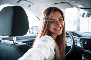 Selfies machen. Fröhliche Fahrerin ist in ihrem neuen Auto. Innenraum des modernen Automobils foto