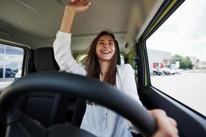 glücklicher Besitzer. Vorderansicht der Frau, die modernes neues Auto in der Stadt fährt foto