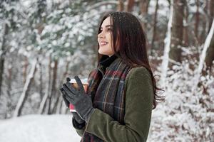 Dieses Getränk wird Sie in der stärksten Kälte wärmen. Mädchen mit einer Tasse Kaffee spazieren im Winterwald foto