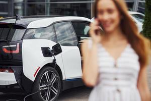 Technik der Bildfokussierung. mit Telefon. Frau an der Ladestation für Elektroautos tagsüber. brandneues Fahrzeug foto