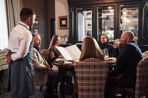 Kellner wartet auf eine Bestellung. Freunde der Familie haben eine schöne Zeit in einem schönen modernen Luxusrestaurant foto