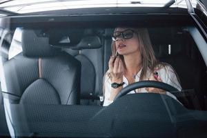 angesehene Geschäftsfrau. schönes blondes mädchen, das im neuen auto mit modernem schwarzem interieur sitzt foto