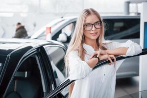 süßes mädchen in brillen steht neben dem auto im autosalon. wahrscheinlich ihr nächster Einkauf foto