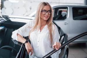 mit Lieferwagen dahinter. süßes mädchen in brillen steht in der nähe des autos im autosalon. wahrscheinlich ihr nächster Einkauf foto