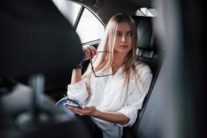 neue Angebote kommen. smarte geschäftsfrau sitzt auf dem rücksitz des luxusautos mit schwarzem interieur foto