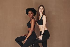 Models. Zwei multiethnische Freundinnen stehen im Studio mit braunem Hintergrund foto