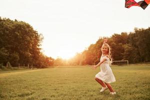 Drachen ist im Himmel. glückliches Mädchen in weißen Kleidern hat Spaß auf dem Feld. schöne Natur foto