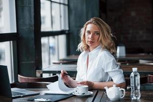 umblättern. Geschäftsfrau mit lockigen blonden Haaren drinnen im Café tagsüber foto
