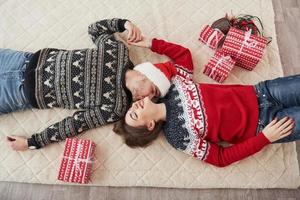 Mann küsst seine Frau. Draufsicht des Paares in Weihnachtskleidung liegt auf dem Boden mit Geschenken darauf foto