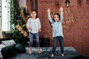 Fröhliche Kinder haben Spaß und springen auf dem Bett mit dekorativem Urlaubshintergrund foto