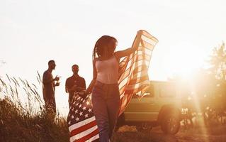 Mädchen rennt nach vorne. freunde haben ein schönes wochenende im freien in der nähe ihres grünen autos mit usa-flagge foto