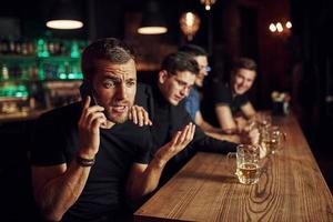 Mann spricht am Telefon. drei Sportfans in einer Bar beim Fußball schauen. mit Bier in der Hand foto