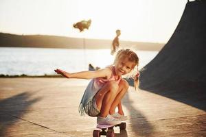 erste Versuche. sonniger Tag. kind viel spaß mit skate an der rampe. fröhliches kleines Mädchen foto