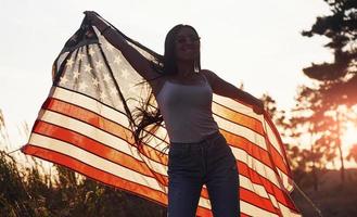 schönes Licht. brünette mit usa-flagge in den händen hat eine gute zeit und fühlt sich an einem sonnigen tag im freien frei foto