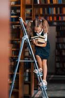Schulmädchen auf der Leiter in der Bibliothek voller Bücher. Bildungskonzeption foto