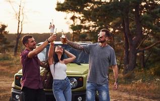 Brille klopfen. eine gruppe fröhlicher freunde hat ein schönes wochenende an einem sonnigen tag in der nähe ihres grünen autos im freien foto