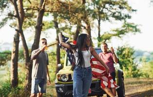 im Wald. freunde haben ein schönes wochenende im freien in der nähe ihres grünen autos mit usa-flagge foto