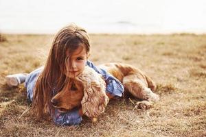 Ruhen in der Nähe des Sees. süßes kleines Mädchen geht an sonnigen Tagen mit ihrem Hund im Freien spazieren foto