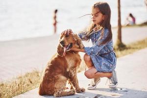 verspielte Stimmung. süßes kleines Mädchen geht an sonnigen Tagen mit ihrem Hund im Freien spazieren foto