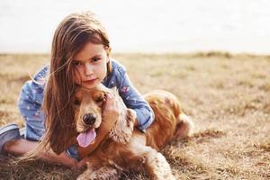 Ruhen in der Nähe des Sees. süßes kleines Mädchen geht an sonnigen Tagen mit ihrem Hund im Freien spazieren foto