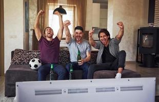 es ist ein Ziel. aufgeregt drei freunde, die zu hause gemeinsam fußball im fernsehen gucken foto